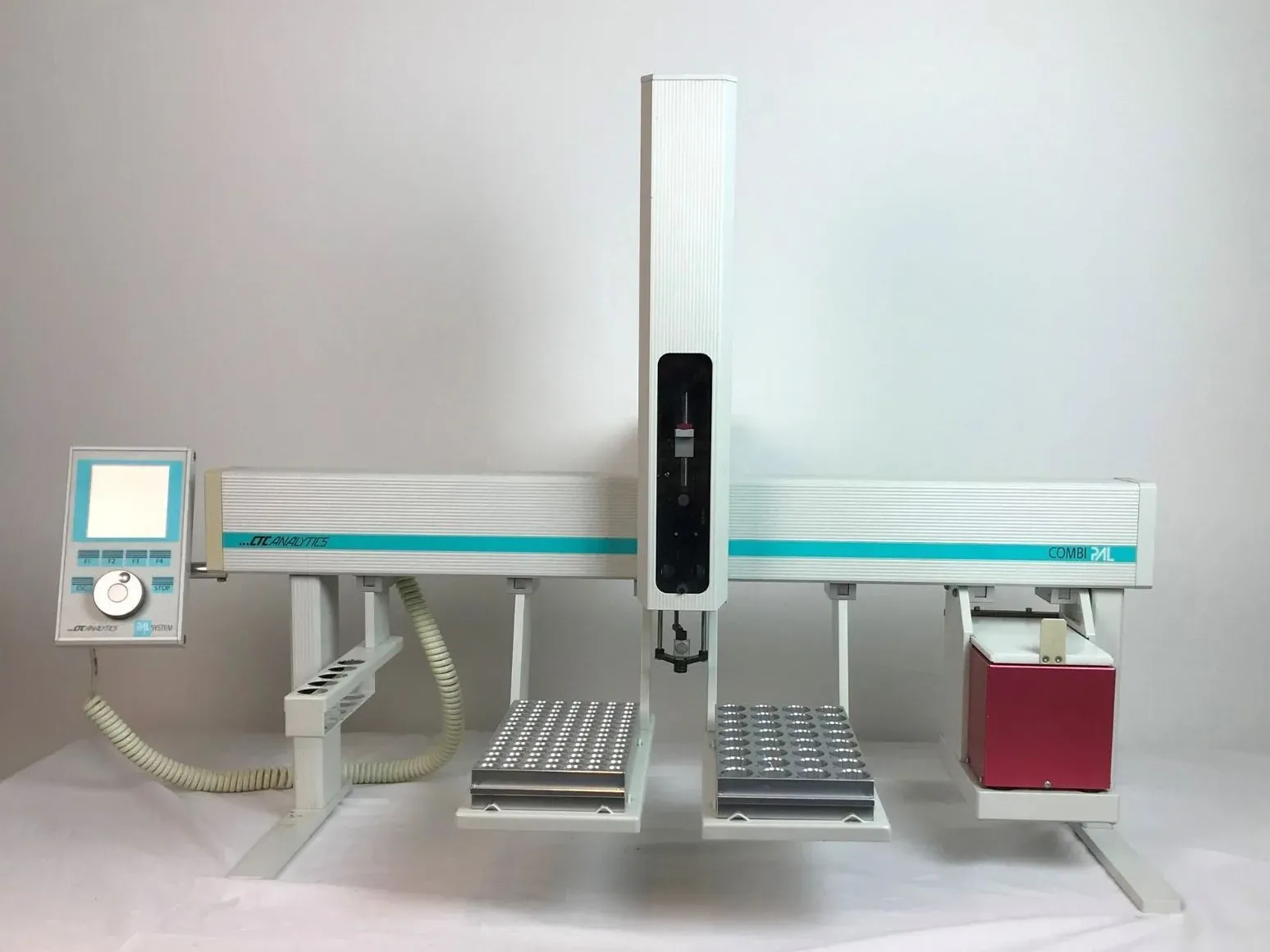 A rail-mounted autosampler: a control pad at one end, a vertical tower carrying a syringe, two trays of sample vials beneath it, and a heated module at the far end.