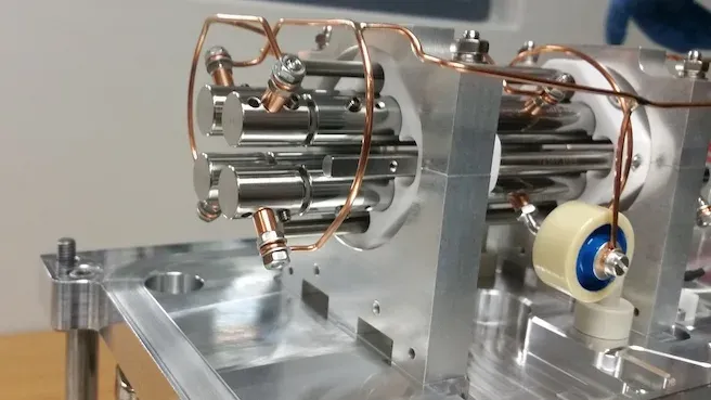 A quadrupole assembly on a machined baseplate: four polished parallel rods held in ceramic insulators, with copper radiofrequency wiring looped over them.